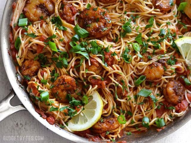 Finished skillet full of Blackened Shrimp Pasta with lemon slices, parsley, and green onion