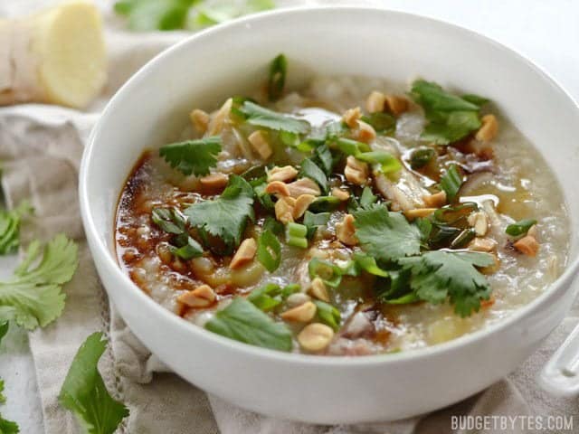 Side view of a bowl full of congee, topped with peanuts, cilantro, and sesame oil