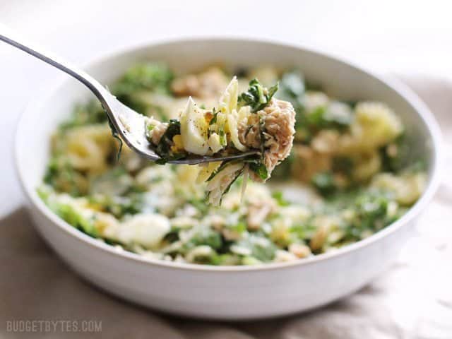 Close up of kale and salmon caesar salad on a fork with the bowl in the background