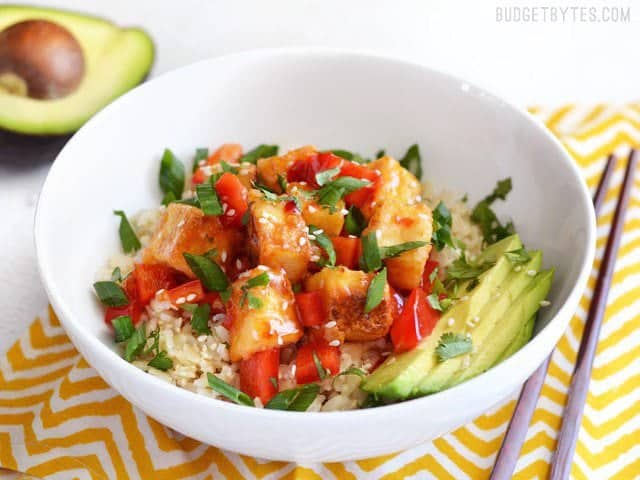 Front view of Sweet Chili Stir Fried Tofu Bowl on a napkin, chopsticks on the side, avocado in the back