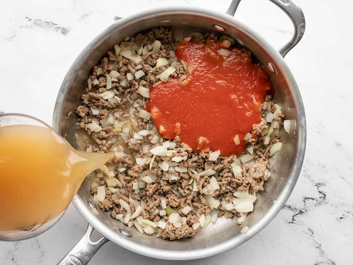 Tomato sauce in the skillet, beef broth being poured in