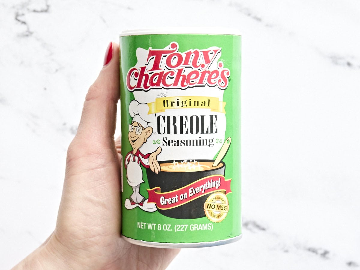 A hand holding a pot of tony chachere creole seasoning.