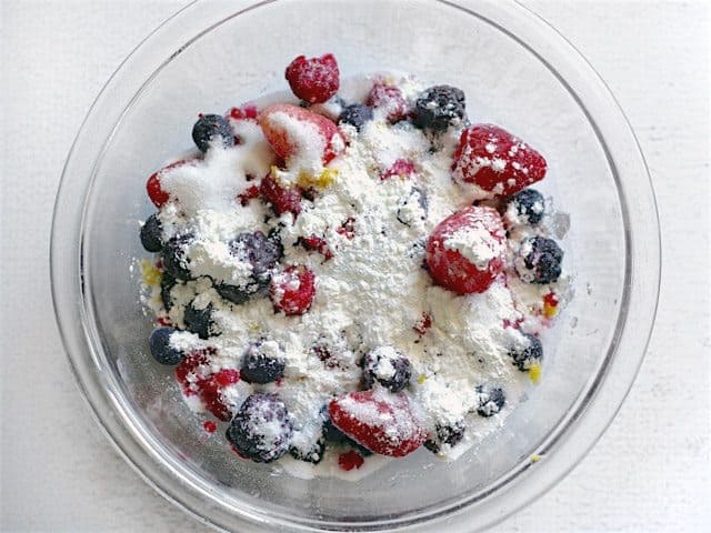 Thawed frozen mixed berries in a bowl with sugar, cornstarch, and lemon zest