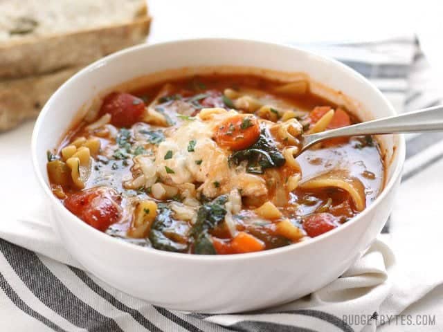 Front view of a bowl full of Garden Vegetable Lasagna soup, a spoon lifting a cheese-filled bite