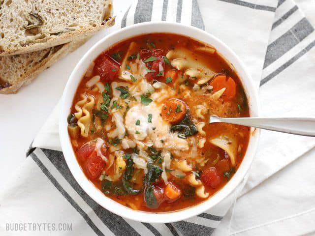 Overhead view of a bowl full of Garden Vegetable Lasagna soup with a spoon in the center, bread on the side