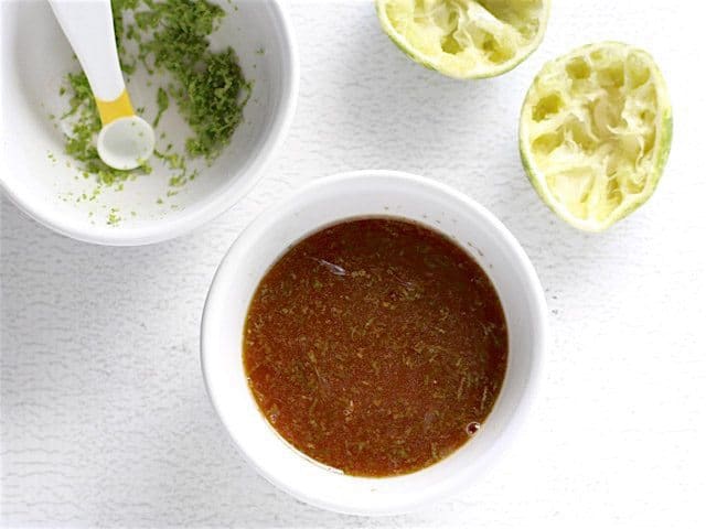 Honey Lime Glaze in a small bowl with squeezed lime and lime zest on the sides