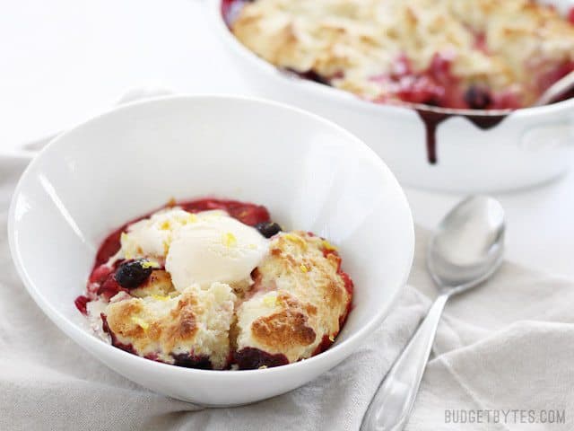 Side view of a bowl full of lemon berry cobbler with the casserole in the back