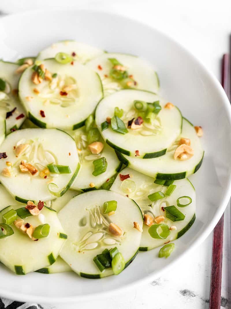 Side view of a bowl full of sesame cucumber salad, chopsticks on the side