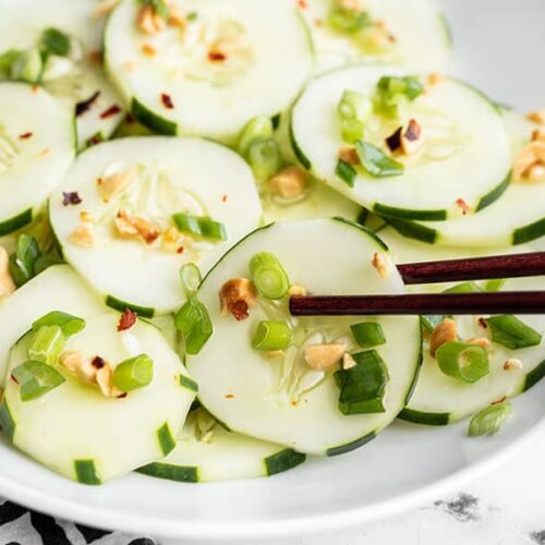 Side view of a bowl of sesame cucumber salad, chopsticks picking up one slice of cucumber