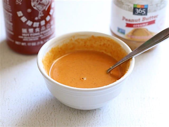 Spicy Peanut Sauce in a small bowl, sriracha and peanut butter in the backround