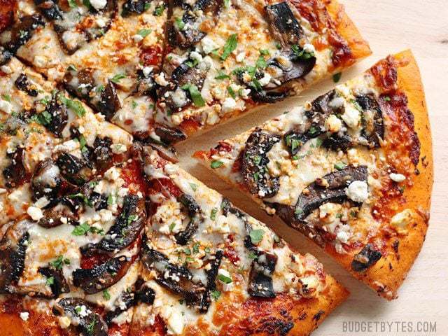 Baked and sliced Ultimate Portobello Mushroom Pizza on a wooden cutting board