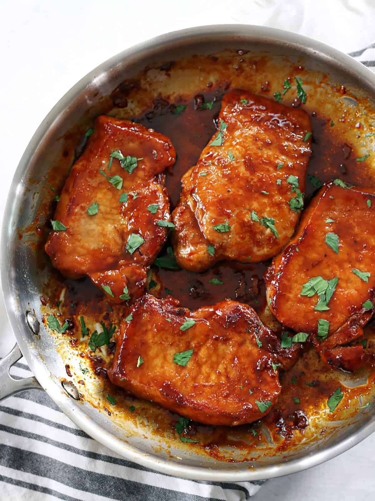 Overhead view of a skillet full of glazed pork chops garnished with parsley.