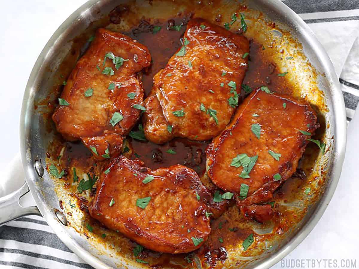 Overhead view of finished brown sugar glazed pork chops in the skillet garnished with parsley.