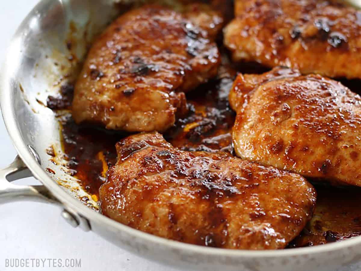 Close up side view of glazed pork chops in a skillet.