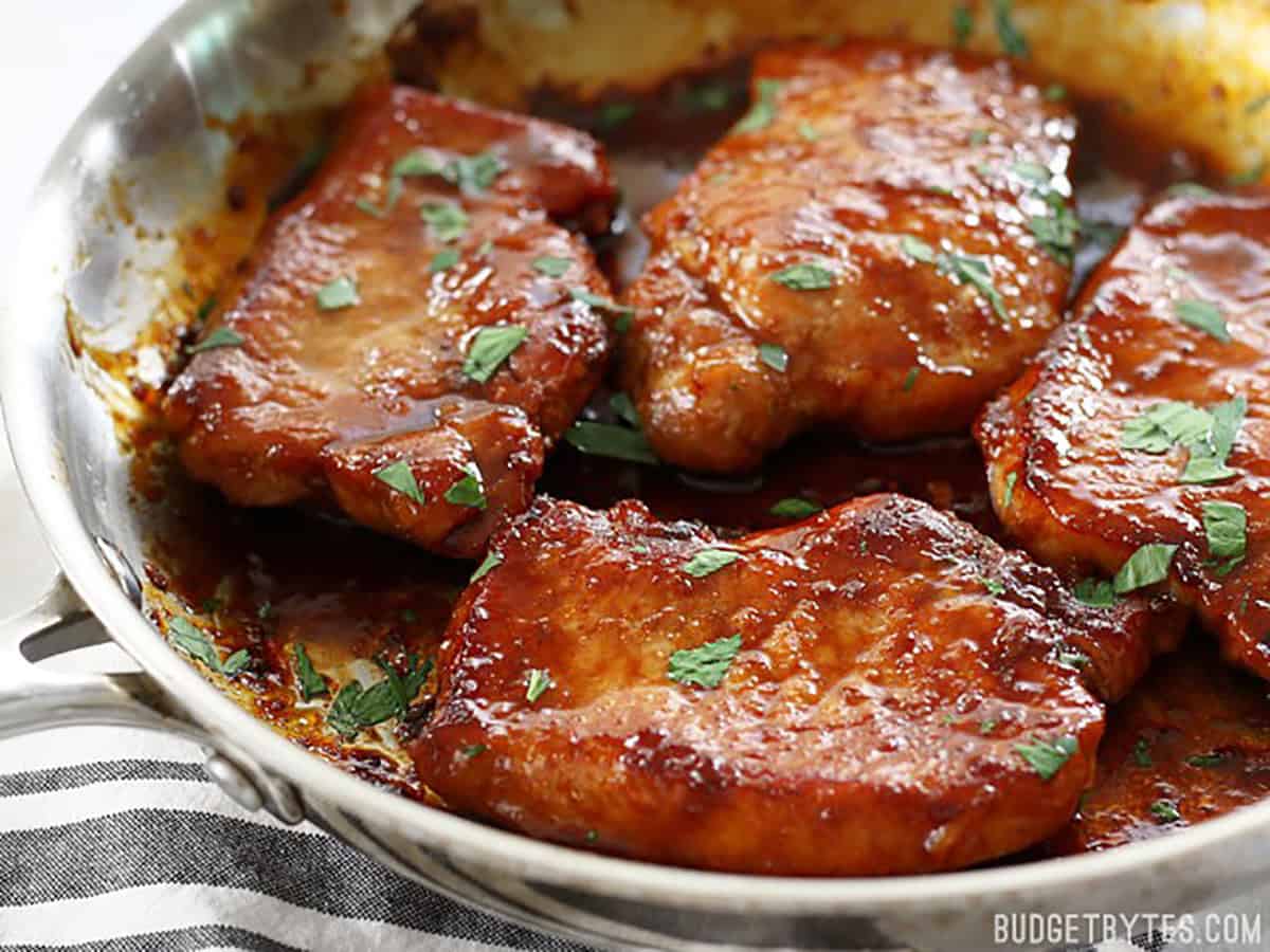 Side view of finished pork chops in the skillet garnished with parsley.