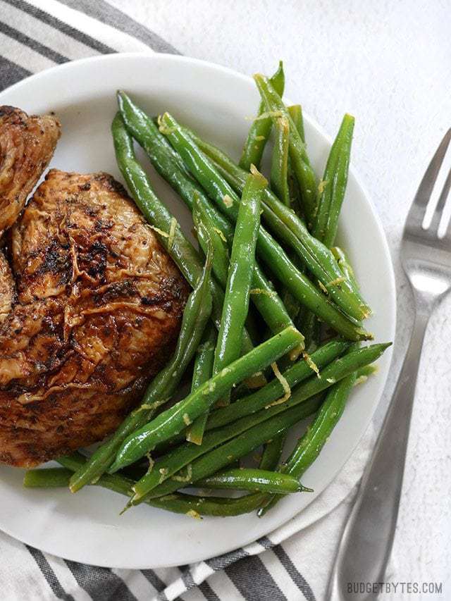 A big pile of lemon butter green beans on a plate with some roasted chicken