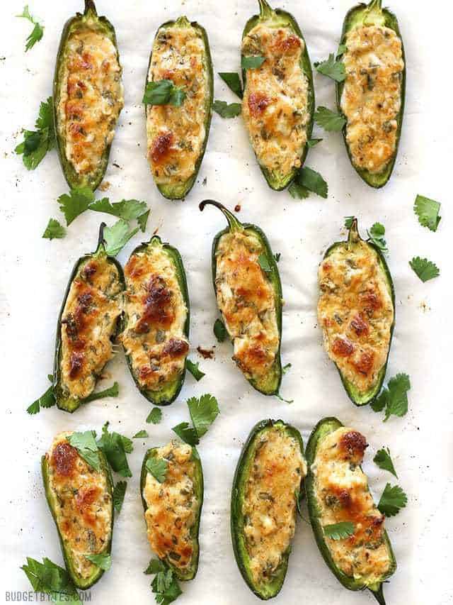 Stuffed Jalapeños viewed from above lined up on a piece of parchment paper, garnished with cilantro