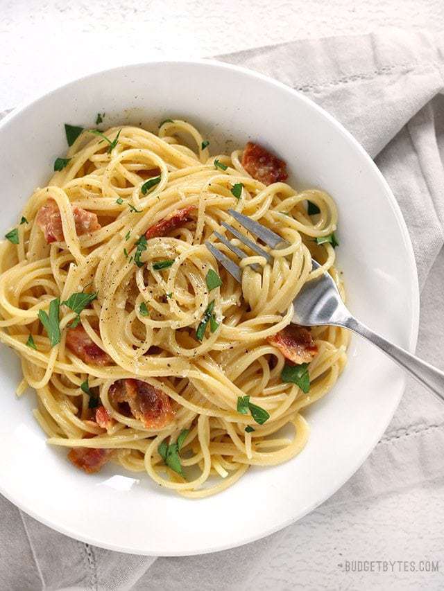 Overhead view of a bowl of Spaghetti Carbonara garnished with parsley and the fork twirled into the spaghetti