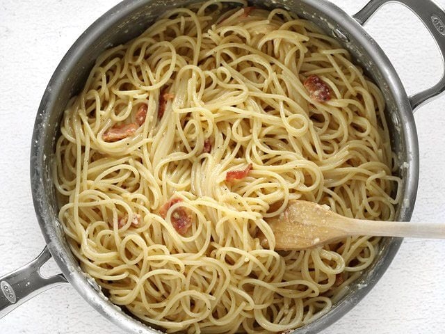 Finished skillet full of spaghetti carbonara with a wooden pasta fork