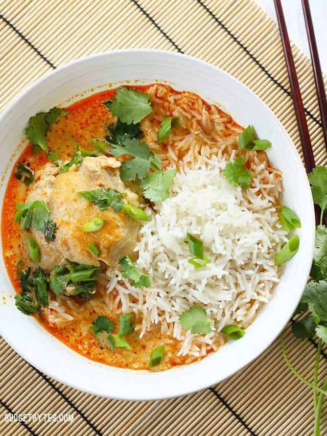 Overhead view of a bowl full of Thai Curry Chicken Thighs with jasmine rice and cilantro. Chopsticks on the side.