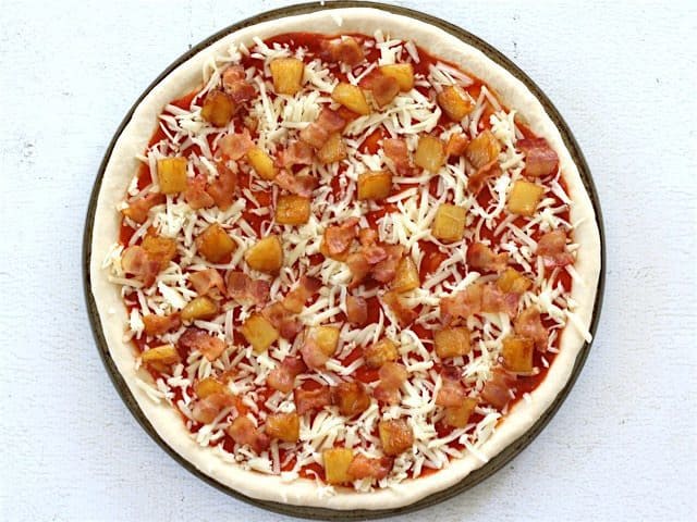 Uncooked pizza topped with cooked bacon and caramelized pineapple