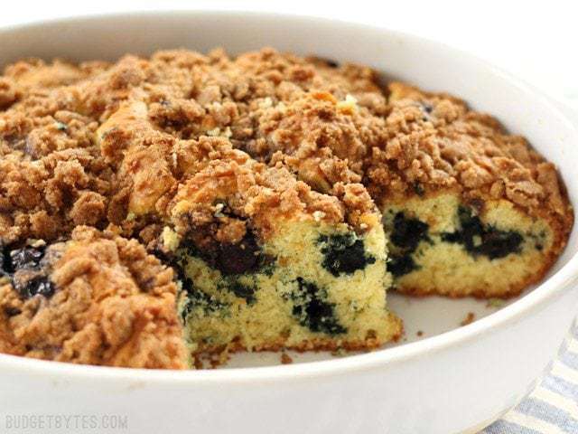 Side view of a Blueberry Buttermilk Coffee Cake with pieces cut out so you can see the crumb and juicy blueberries inside