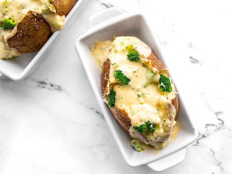 Overhead view of a broccoli cheddar stuffed potato in an individual white ceramic casserole dish