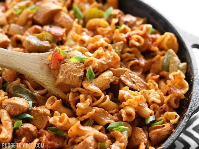 Close up of a wooden spoon scooping some Creamy Chicken Fajita Pasta out of the skillet