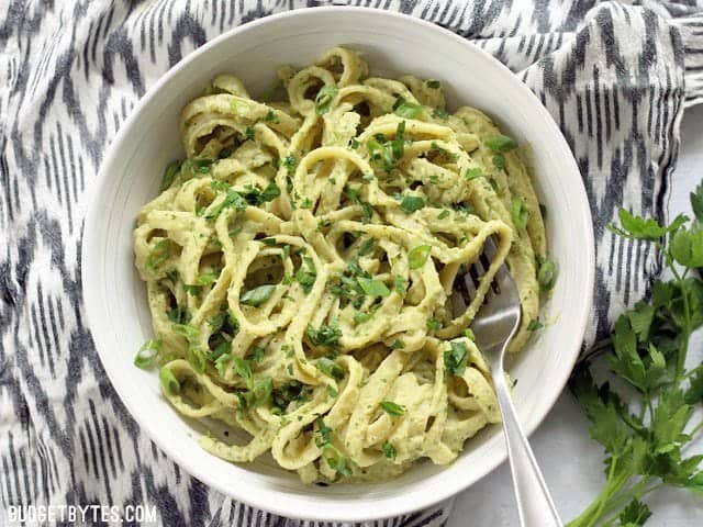 A finished bowl of Parsley Scallion Hummus Pasta on an ikat napkin with parsley on the side