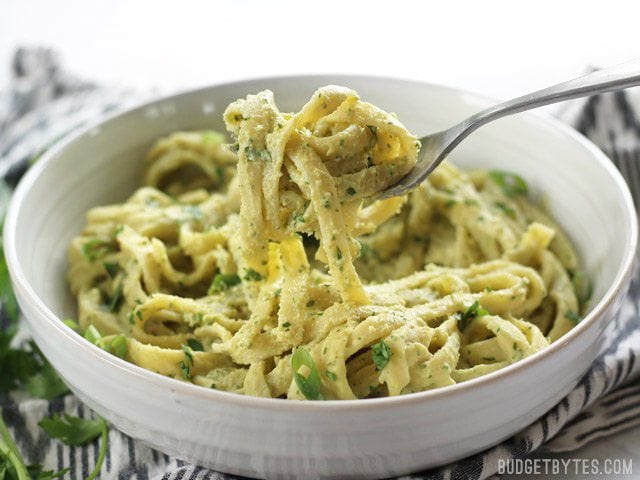 A fork lifting some Parsley Scallion Hummus Pasta out of the bowl, viewed from the side