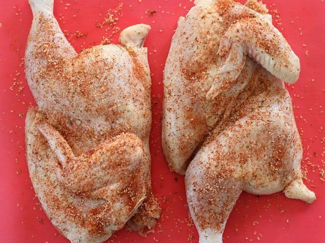 Split Chicken seasoned with spices on a red cutting board