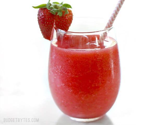 Side view of a Strawberry Rosé Slush with a pink paper straw and fresh strawberry on the rim.