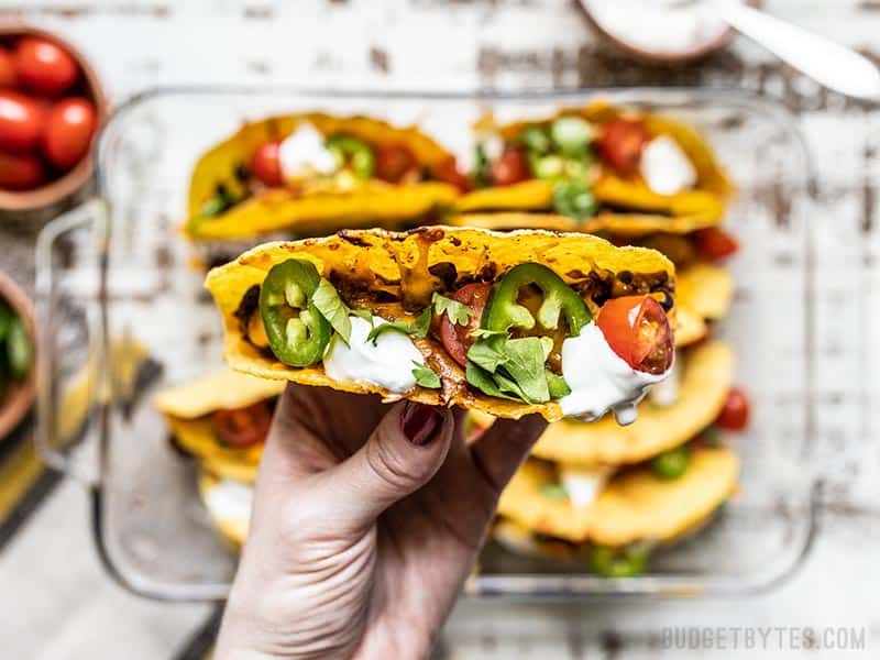 One Baked Beef and Black Bean Taco being held close to the camera, with the rest of the tacos in the background.