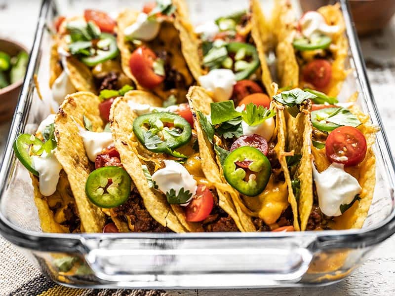 Tacos topped with fresh tomato, cilantro, jalapeños, and sour cream. Side view.