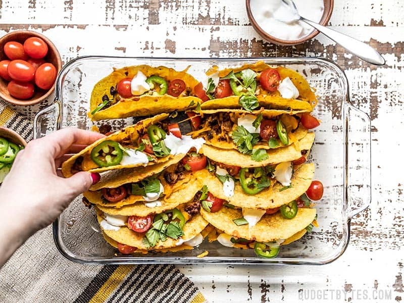 A hand picking up one of the baked beef and black bean tacos out of the casserole dish