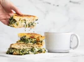 A hand picking up a piece of spinach artichoke grilled cheese with cheese stretching from the slice