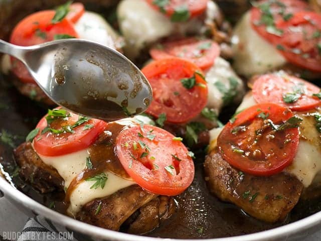 Balsamic glaze being drizzled over a piece of chicken with mozzarella and tomatoes