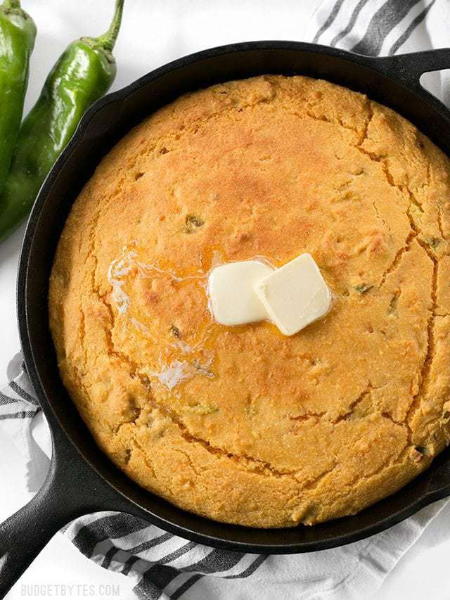 Top view of Hatch Chile Sweet Potato Cornbread in cast iron skillet with two cubes of butter on top 