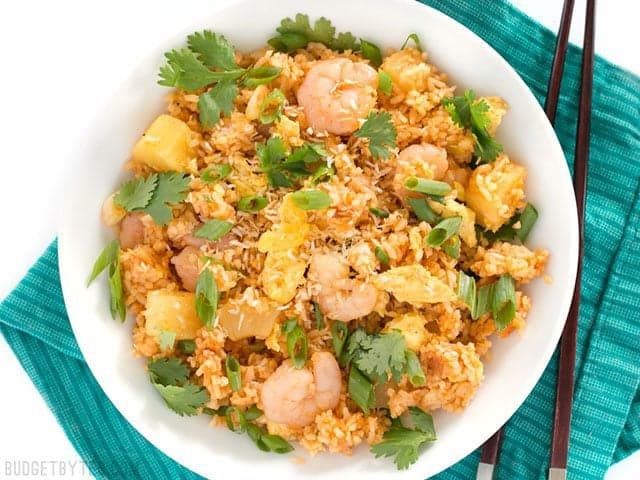 Overhead view of a bowl of Shrimp Fried Rice with Pineapple and Toasted Coconut on a teal napkin