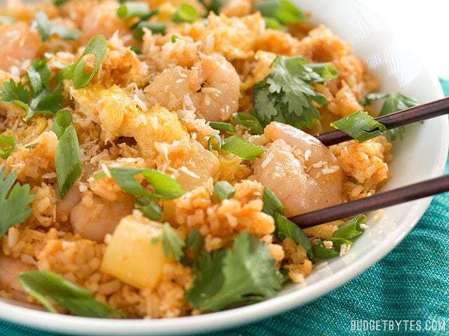 Close up side view of a chopsticks picking up a piece of shrimp from a bowl of Shrimp Fried Rice with Pineapple and Toasted Coconut 