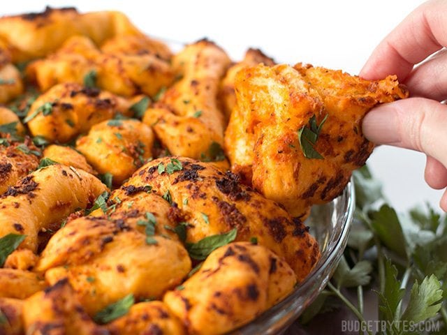 Close up of a hand pulling a piece of Tomato Herb Pull Apart Bread from the baking dish.