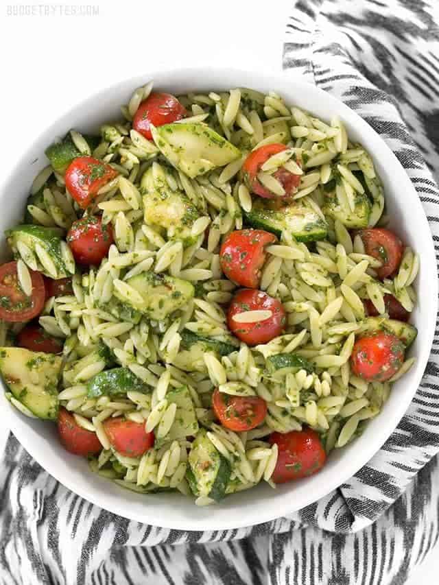 Overhead view of a bowl full of Zucchini and Orzo Salad with Chimichurri, on a black and white striped napkin