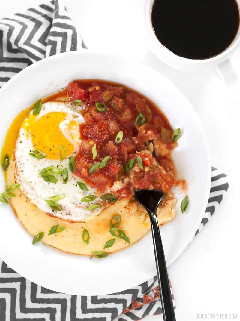 A Cheddar Grits Breakfast Bowl on a striped napkin, being eaten with a black fork