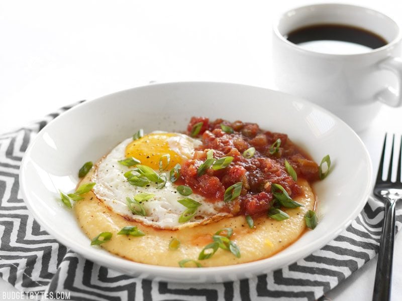 Front view of a Cheddar Grits Breakfast Bowl with a cup of coffee behind it