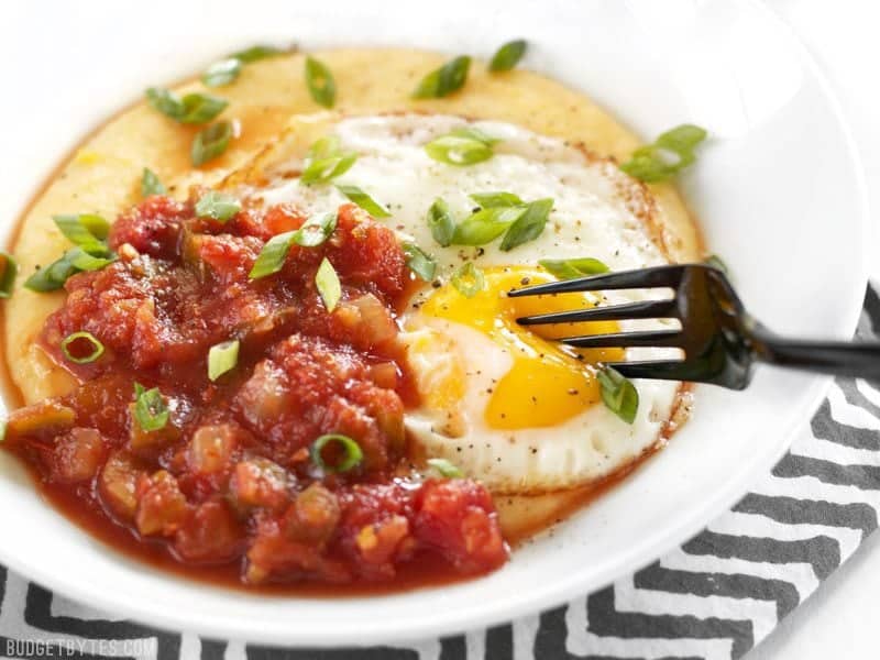 The yolk of an egg in a Cheddar Grits Breakfast Bowl being pierced with a fork.