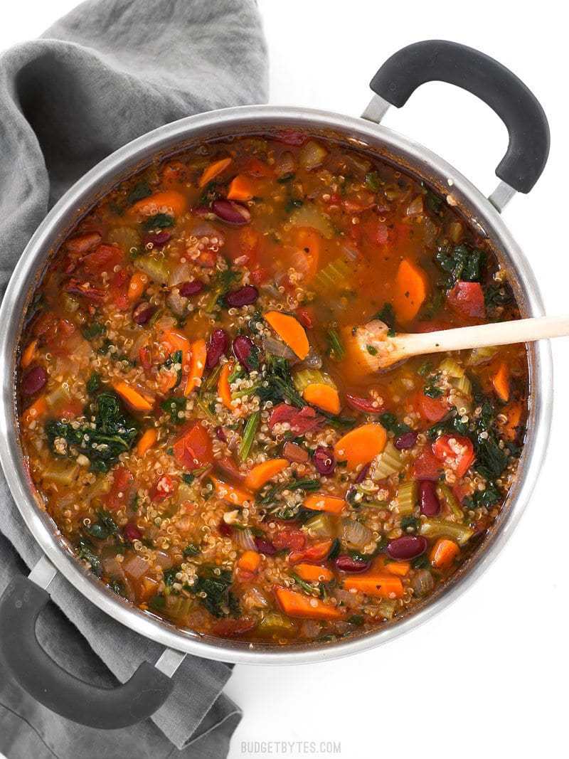 Overhead view of a pot full of Garden Vegetable Quinoa Soup with a wooden spoon stuck in the middle