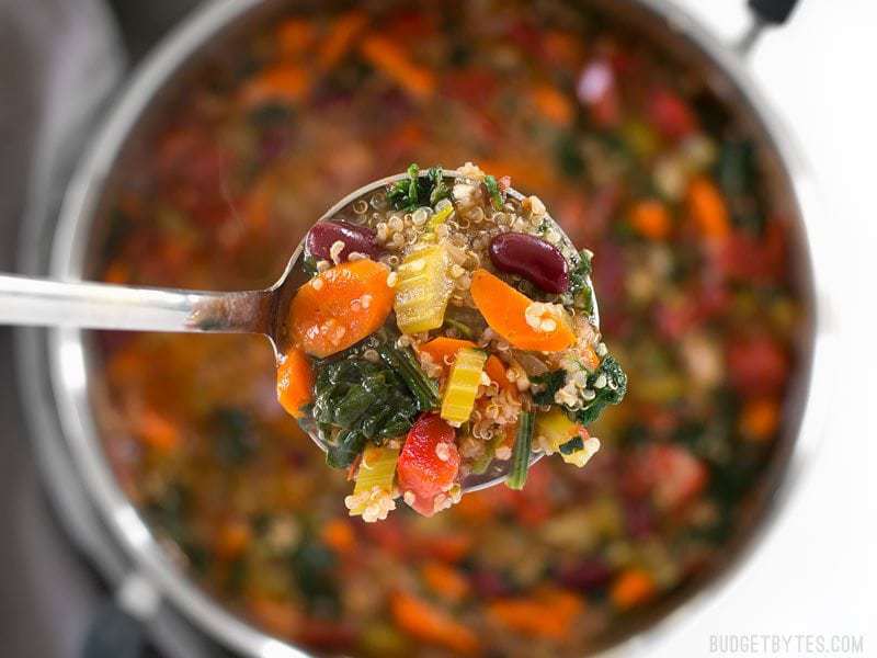 Close up of a ladle full of Garden Vegetable Quinoa Soup with the pot in the background