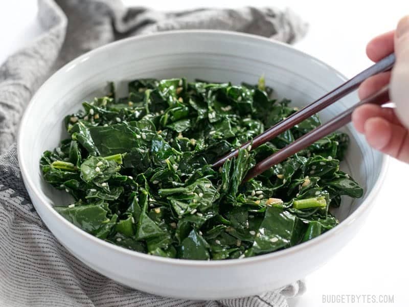 Front view of Sesame Kale being picked up with chopsticks out of the bowl