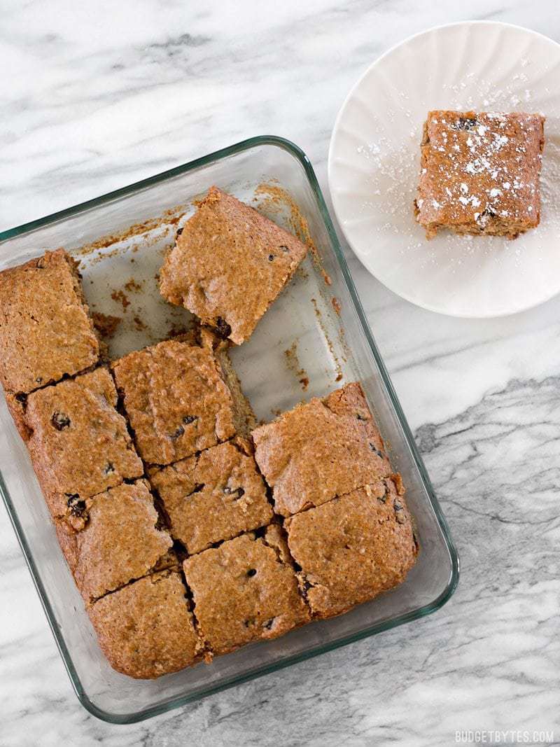 Applesauce Cake cut into squares, one square on a small plate o the side, dusted with powdered sugar