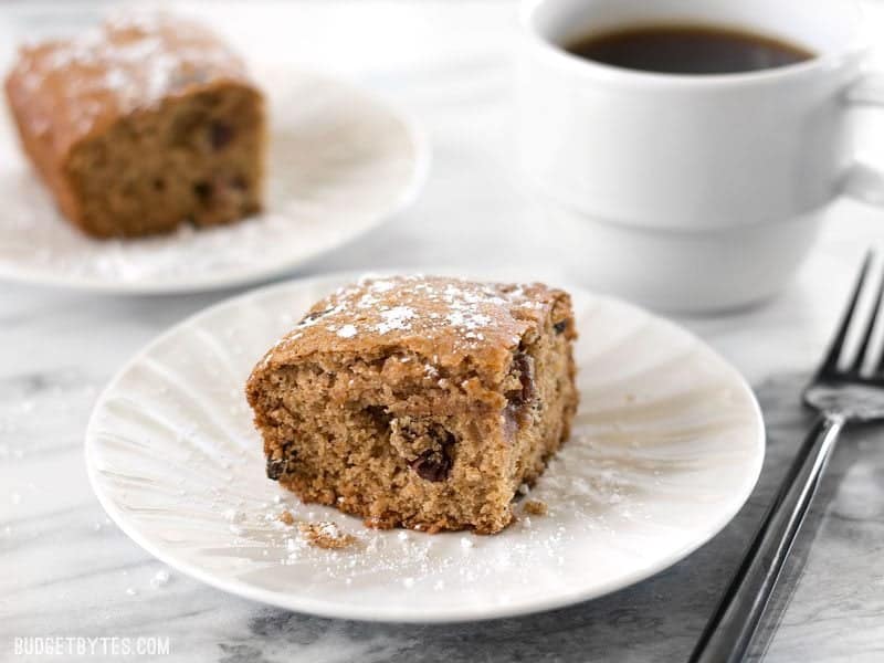 Close up of one slice of Applesauce Cake with a second slice and cup of coffee in the background